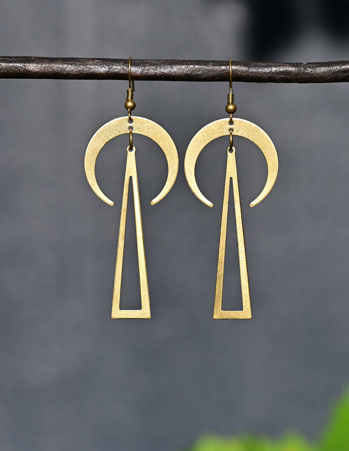 Brass earrings with geometric design hanging on a branch against a dark background